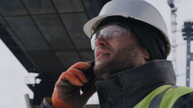 Erkek işçi yarım kalmış köprünün altında telefona cevap veriyor.