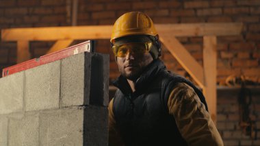 Erkek inşaatçı tuğla duvarın arkasında.
