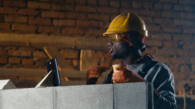 Siyahi inşaatçı öğle arasında video görüşmesi yapıyor.