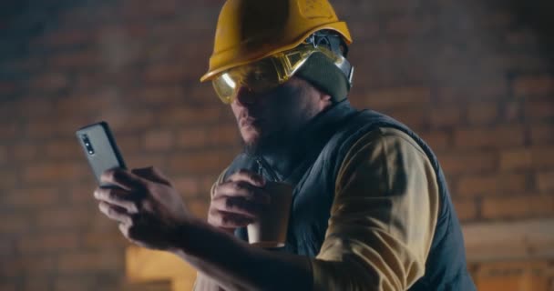 Construtor masculino com bebida quente usando smartphone — Vídeo de Stock