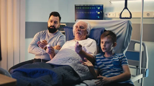 Uomo anziano che celebra la vittoria della squadra preferita con figlio e nipote nel reparto ospedaliero — Foto Stock