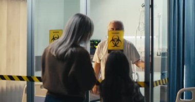 Cam duvardan ziyaretçilerle iletişim kuran kıdemli bir hasta.