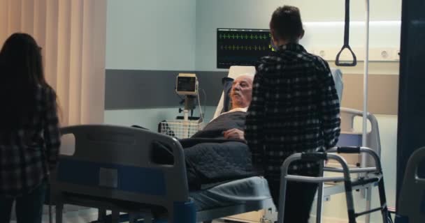 Врач и семья, посещающие пожилого человека в клинике — стоковое видео