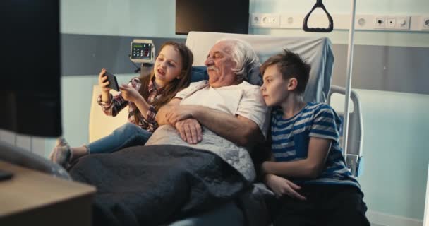 Starší pacient diskutuje o videu na smartphonu s vnoučaty v nemocničním oddělení — Stock video