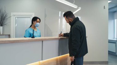 Erkek hasta klinik resepsiyonunda sözleşme imzalıyor.