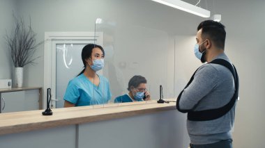 Maskeli Asyalı resepsiyonist hastanedeki yaralı hastaya yardım ediyor