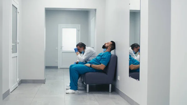 Αγχωμένοι άνδρες γιατροί κάθονται στον καναπέ στην κλινική διάδρομο — Φωτογραφία Αρχείου