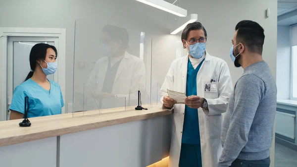 Различные медсестра и врач, помогающие пациенту мужского пола на ресепшене — стоковое фото