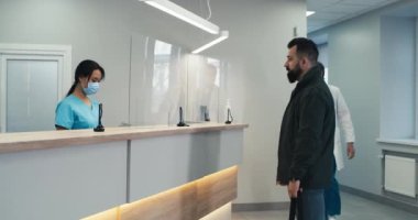 Sakallı hasta resepsiyondaki doktor ve hemşireyle iletişim kuruyor.
