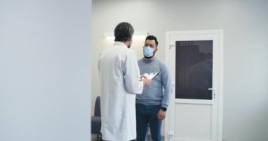 Erkek doktor hastane koridorunda hastayla konuşuyor.