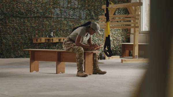 Spor salonunda akıllı telefon kullanan siyah asker kadın. — Stok fotoğraf