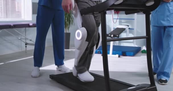 Homme en exosquelette marchant sur tapis roulant près des thérapeutes de réadaptation — Video