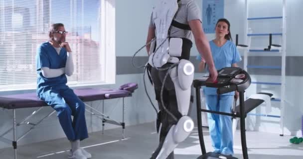 Mužští a ženští terapeuti kontrolující rehabilitaci člověka v exoskeletonu — Stock video