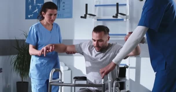 Niepełnosprawny człowiek próbuje spacerować z ramą spacerową w pobliżu lekarzy — Wideo stockowe