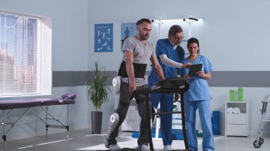 Doktorlar dış iskeletteki hastanın yakınındaki rehabilitasyon sonuçlarını tartışıyor