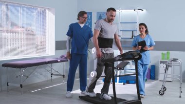 Doktorlar dış iskeletteki hastanın yakınındaki rehabilitasyon sonuçlarını tartışıyor