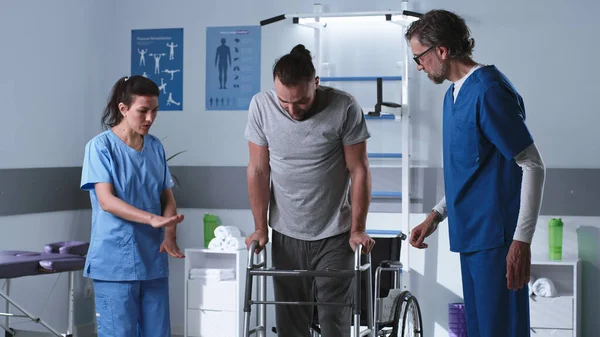 Инвалид пытается прогуляться с ходячей рамой рядом с врачами — стоковое фото