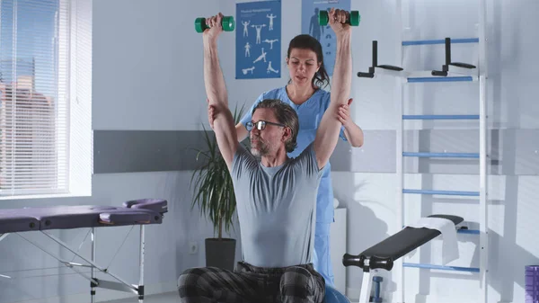 Terapeuta que ayuda a la paciente a hacer ejercicio con pesas — Foto de Stock