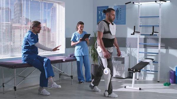 Uomo in esoscheletro imparare a camminare sul tapis roulant vicino ai medici — Foto Stock