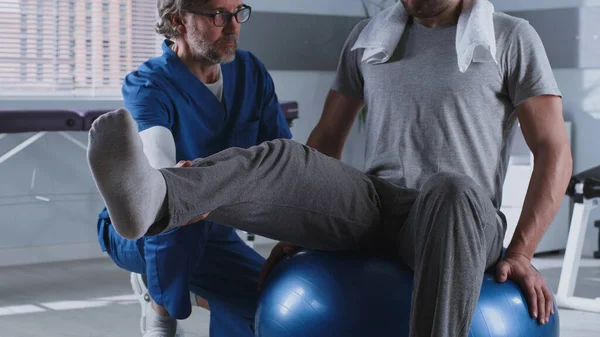 Terapeuta de rehabilitación madura ayudando a paciente en la bola en forma — Foto de Stock