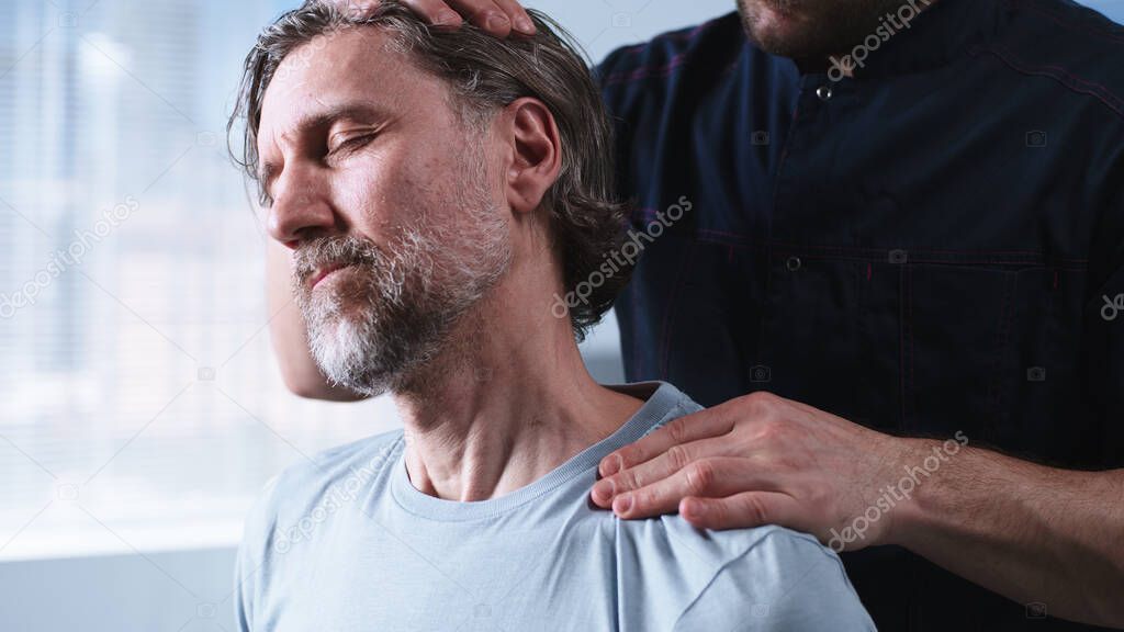 Crop therapist stretching neck of middle aged man