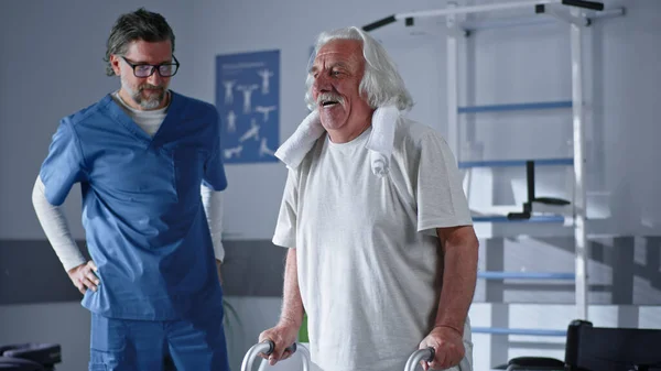 Щасливий старший пацієнт використовує пішохідну рамку біля лікаря — стокове фото