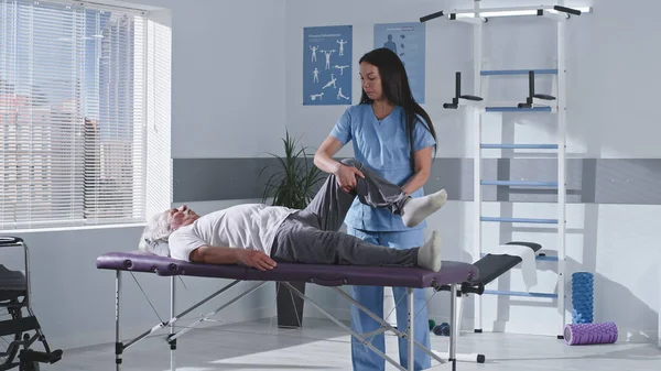 Reha-Therapeut streckt Bein eines älteren Patienten — Stockfoto