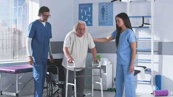 Terapisti riabilitativi che insegnano all'uomo anziano a passeggiare con il telaio — Foto Stock