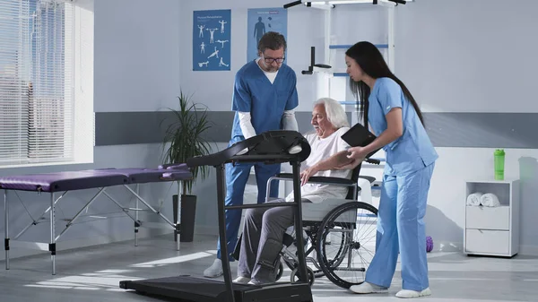 Terapisti della riabilitazione che aiutano il paziente anziano a camminare sul tapis roulant — Foto Stock