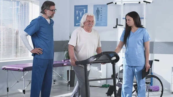 Rehabilitasyon terapistleri yaşlı hastaların koşu bandında yürümesine yardım ediyor. — Stok fotoğraf