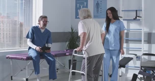 Skadad senior patient som går mot rehabiliteringsterapeuter — Stockvideo