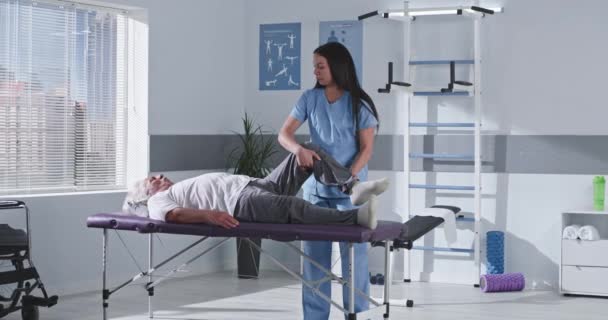 Thérapeute de réadaptation étirement jambe du patient âgé — Video