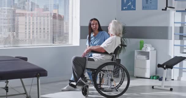 Vänlig rehabiliteringsterapeut som talar med handikappade äldre patienter — Stockvideo