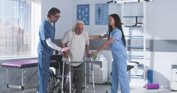 Terapeuci rehabilitacyjni uczą starszego człowieka chodzić z ramą spacerową — Wideo stockowe