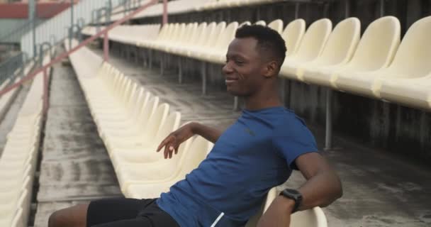 Щасливий чорний спортсмен відпочиває на стадіоні — стокове відео