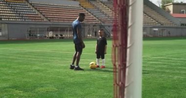 Zenci koç, çocukla stadyumda futboldan bahsediyor.