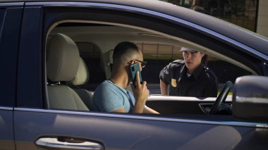 Akıllı telefonlu sinirli sürücü polis memuruyla konuşuyor.