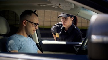 Kadın polis, erkek sürücü belgelerini inceliyor.