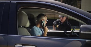 Akıllı telefonlu sinirli sürücü polis memuruyla konuşuyor.