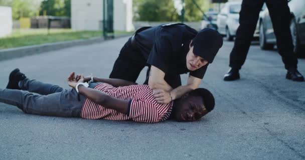 Boze politieagent ondervraagt Afro-Amerikaanse man op de grond — Stockvideo