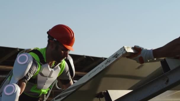 Mužský technik v exoskeletu instalující solární článek s kolegou — Stock video