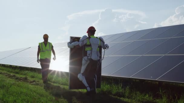 Manlig tekniker i exoskelett transporterar solpanel till medarbetare — Stockvideo