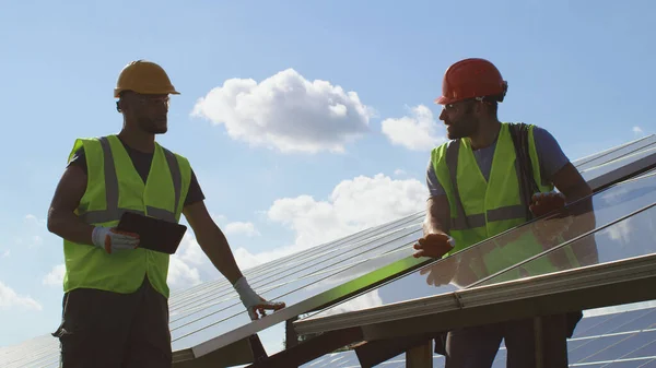 Ingenieros masculinos examinando paneles fotovoltaicos en día soleado —  Fotos de Stock