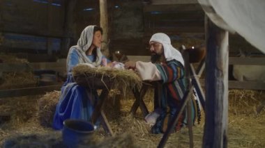 Meryem ve Yusuf konuşuyor ve bebek İsa 'ya bakıyorlar.