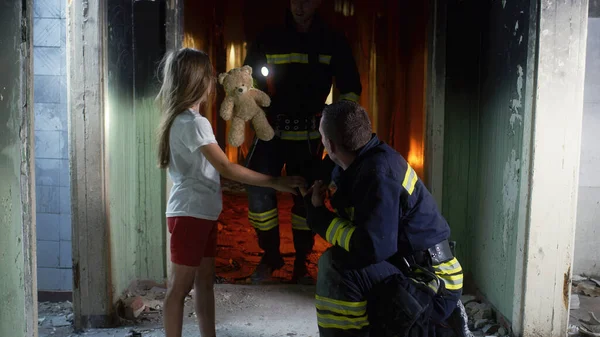 Brandweermannen spreken en geven speelgoed aan meisje — Stockfoto