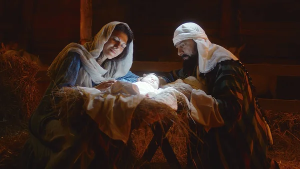 Maria e José acariciando o bebê Jesus na manjedoura iluminada — Fotografia de Stock