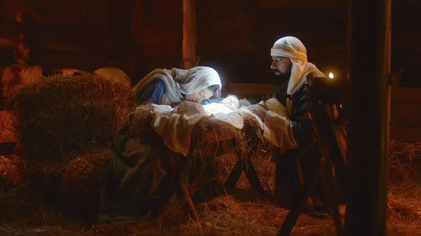 Maria e José acariciando o bebê Jesus na manjedoura iluminada — Fotografia de Stock