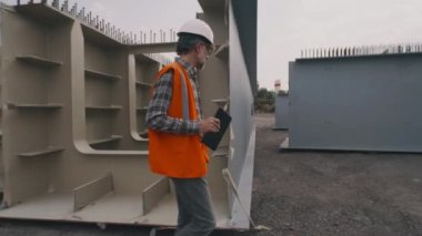 Metal parçalarının yanında yürüyen orta yaşlı mühendis
