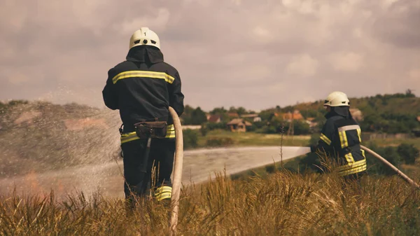 Firemen extinguishing fire in meadow — Stock Photo, Image