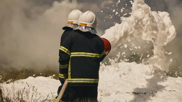 Firemen extinguishing fire in field — Stock Photo, Image
